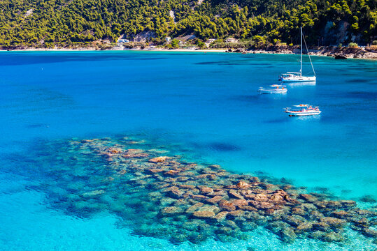 Fototapeta Rocks and stones in crystal clear turquoise sea water of Agios Nikitas bay with sailing boats, Lefkada island, Greece