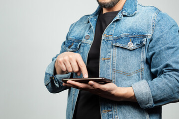 a man at the right side of the screen wearing a denim jacket pointing with his right hand to a mobile phone and a white background