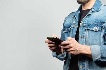 a man wearing a blue denim jacket at the right side of the screen holding an smartphone with both...