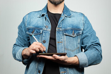 a man wearing a blue denim jacket ready to draw something with a digital pen into a smartphone screen
