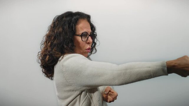 Hispanic woman with curly hair wearing glasses and a sweater making a pulling gesture on isolated white background.