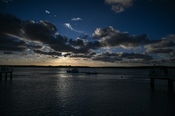 Obraz premium fishing boat on calm water, tropical beach and colorful sunset sky, serene landscape coastal view with wooden pier, cloudy evening, travel and nature tranquility horizon with green vegetation