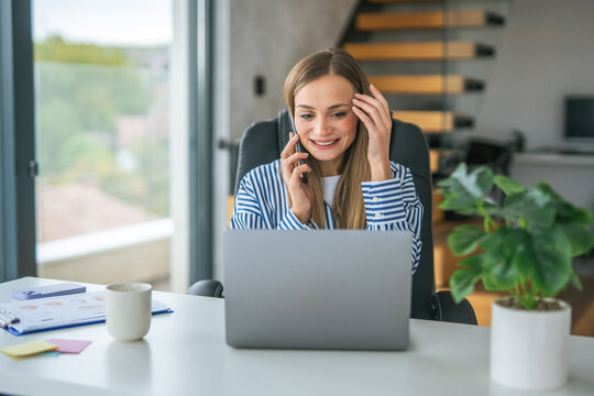 Young woman smiling, multitasking with a phone call and laptop
