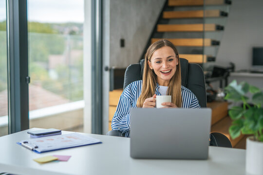 Young woman working from home using laptop and drinking coffee - Powered by Adobe