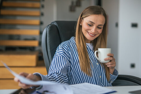 Woman working from home reviewing documents drinking coffee - Powered by Adobe