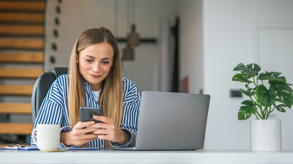 Woman working from home office using laptop and phone