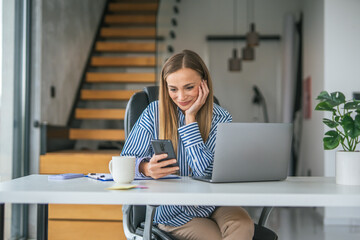 Woman smiling using smart phone at home office desk enjoying remote work
