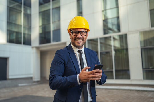 Smiling engineer using smart phone, checking construction project updates