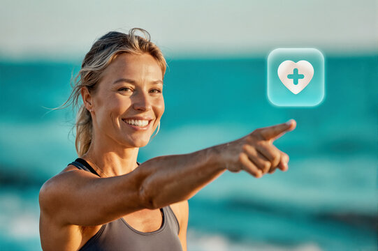 A smiling woman in athletic wear pointing at a digital health app icon against a beach backdrop, photo. - Powered by Adobe