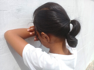 Fototapeta premium Asian girl playing Hide-and-seek. Young girl counting with closed eyes and leaning her arms against a white wall as if hiding while playing hide-and-seek. With copy space