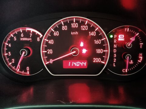 Close-up of a car's dashboard at night, illuminated with a vibrant red glow, featuring the speedometer, tachometer, fuel, and temperature gauges, highlighting vehicle metrics.