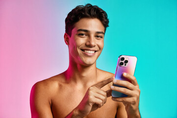 A smiling young man holding a colorful smartphone, pointing at its screen against a vibrant pink and blue gradient background.