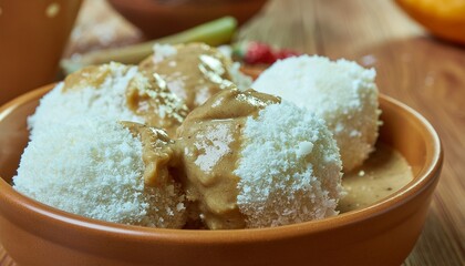 Delicious white dessert dumplings topped with rich peanut sauce and a generous sprinkle of fresh coconut flakes in a rustic bowl, offering a delightful treat