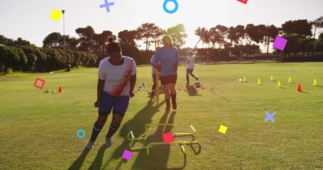 Training women in white jerseys, blue shorts navigating low hurdles on grass at sunset with cones