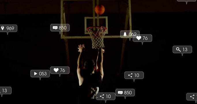 Jumping backlit male athlete reaching toward hoop at gym, with basketball, jersey, social alerts