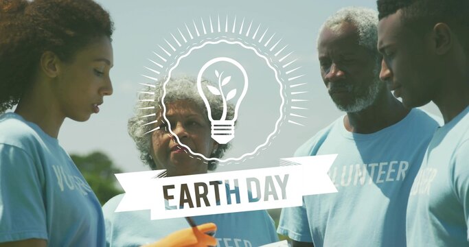 Naklejki Uniting team checking list in park in blue VOLUNTEER tees with orange gloves near EARTH-DAY banner
