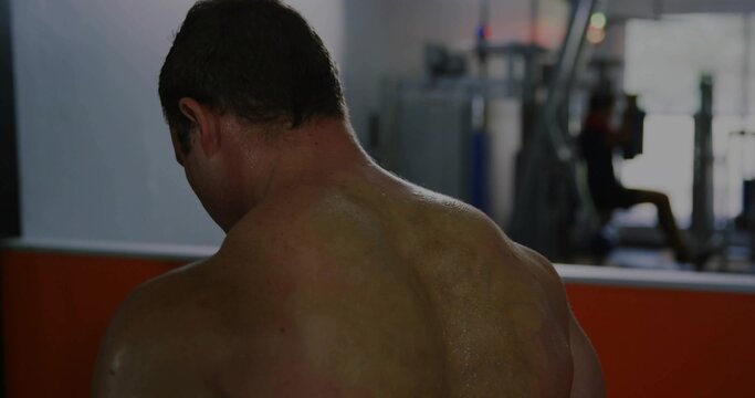 Standing shirtless man flexing back muscles at gym, with mirrored wall and weight machine