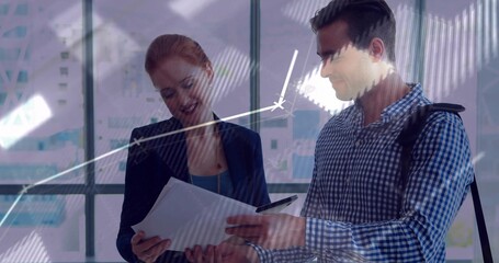 Reviewing two colleagues examining papers near glass windows, navy blazer and checked shirt, chart