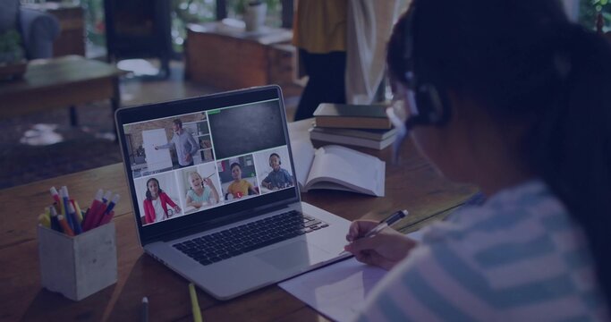 Writing child in striped top wearing headset at wood table, using laptop, notebook, pen, copy space