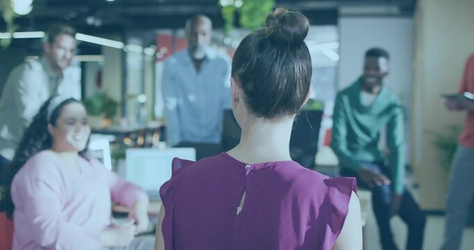 Leading woman wearing sleeveless purple top high bun addressing team in open-plan office tablet