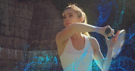 Swinging female tennis player in white tank top, extending racket at outdoor court with blue trails