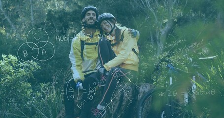 Fototapeta premium Sitting couple wearing yellow jackets leaning on stump in forest with mountain bikes, equations