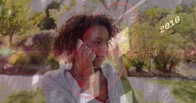 Holding smartphone, woman in cardigan and red top talking in sunlit garden with HUD 2010 graphics - Powered by Adobe