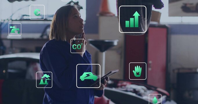 Inspecting female technician in blue coveralls reviewing AR icons in garage, tablet and car on lift