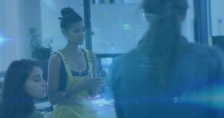 Speaking woman in yellow overalls gesturing and addressing team at open-plan office, with monitors