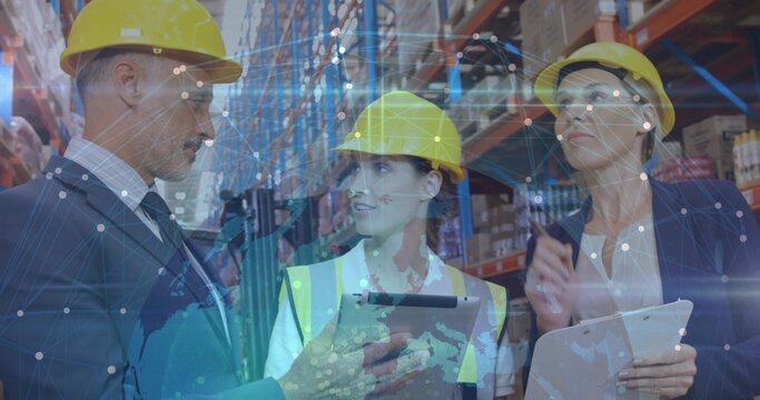 Reviewing 3 warehouse staff checking stock in depot aisle, wearing helmets, suit, vest, overlay - Powered by Adobe