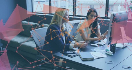 Collaborating two mature women in business casual reviewing papers at desk, with monitor overlay