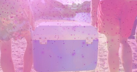 Holding portable cooler, two men wearing floral and coral swim shorts standing at sandy beach