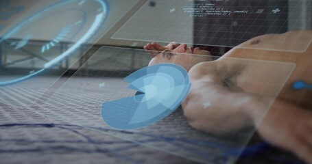 Lying shirtless male being monitored on textured mat in studio, holo UI, blue cord, towel, code