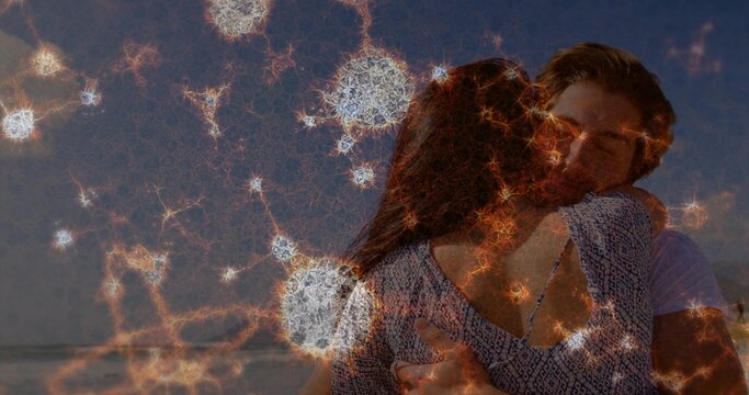 Embracing couple wearing patterned top and pale shirt hugging on beach at sunset, with web overlay