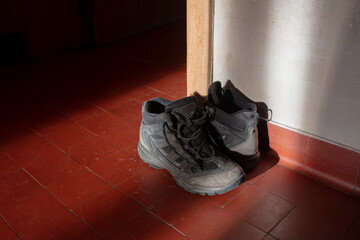 Worn black walking shoes placed by white wall on red ceramic tile floor