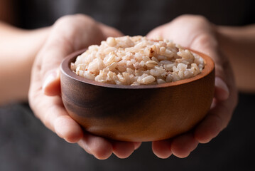 Fototapeta premium Cooked Thai brown rice in a wooden bowl holding by hand, Healthy eating
