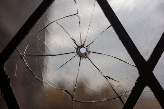Close view of projectile impact point showing radial fracture pattern in diamond lattice window