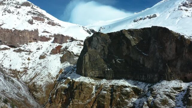 aerial view of the snow covered peaks and rocky slopes of the North Caucasus mountains in Russia. The footage captures the majestic beauty and rugged terrain of this remote and picturesque region duri