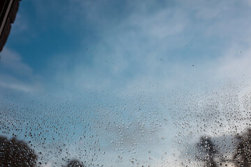 Close view of raindrops on car window creating organic pattern against cloudy sky backdrop