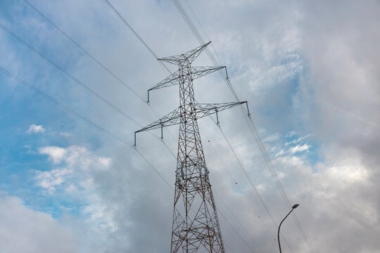 Tall electrical pylon with power lines stretching across cloudy blue sky