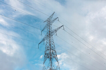 Metal lattice electricity transmission tower against bright blue sky with white clouds