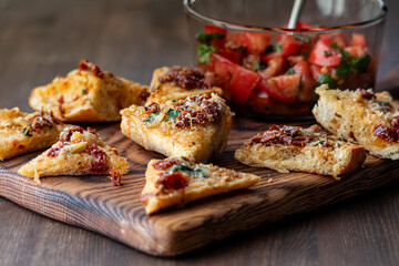 A bowl of bruschetta with toasted baguette pieces in front on a wooden board.
