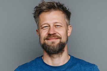 Fototapeta premium Modern portrait of a happy young man radiating positive vibes in simplicity. Real life. Portrait of a young guy in a blue shirt against a gray canvas of simplicity. Daily life. Real moment.
