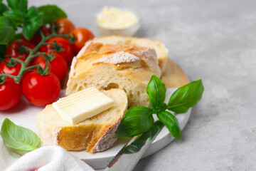 Slices of baguette with butter, basil and tomatoes on light grey table, closeup. Space for text