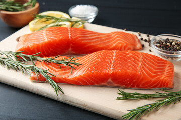 Pieces of salmon fillet, spices and lemon on black wooden table, closeup