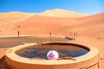 Tourist woman enjoying a thermal pool with therapeutic properties in Empty Quarter desert. Rub' al...