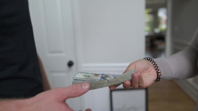 an individual transfers funds in corridor setting, someone provides monetary exchange to companion within enclosed passage, person offers payment in covered hallway while friend accepts