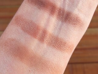 Fototapeta premium Closeup of woman forearm with test of eyeshadow colors. Makeup colors testing on female forearm. Golden, beige, and neutral tones.