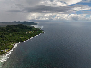 Green hills stretch along the coast under a cloudy sky with waves breaking on the shore. Siargao, Philippines.