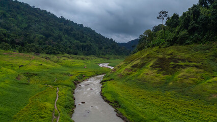 Clear mountain water flows over rocks in a vibrant green valley, surrounded by majestic peaks at dawn.